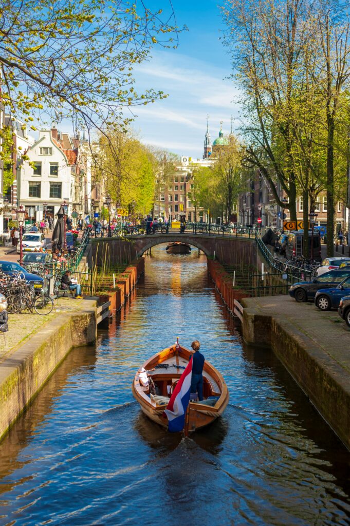 Scenic view of a boat on an Amsterdam canal with people and urban architecture.