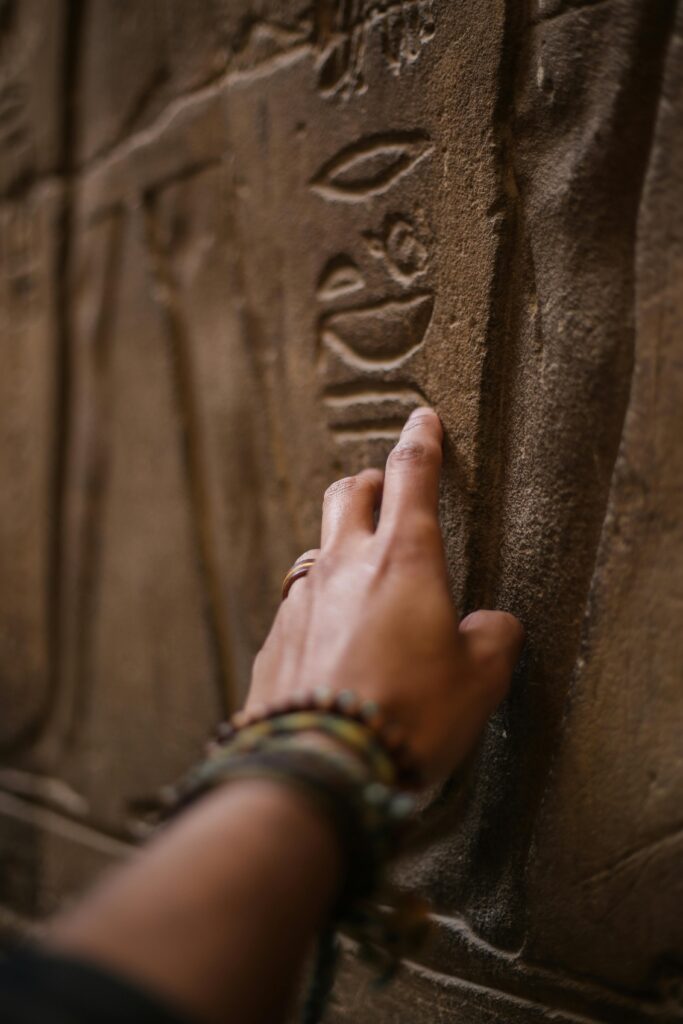 Close-up of a hand touching ancient hieroglyphics on a sandstone wall during an exploration.