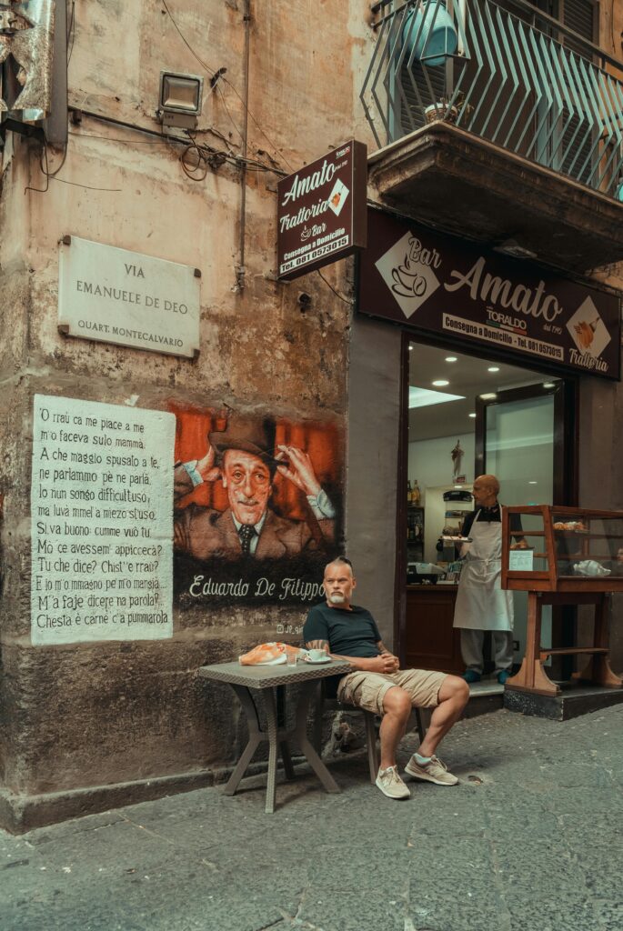 Man relaxing at a cafe in the streets of Napoli, Italy with street art and bakery backdrop.