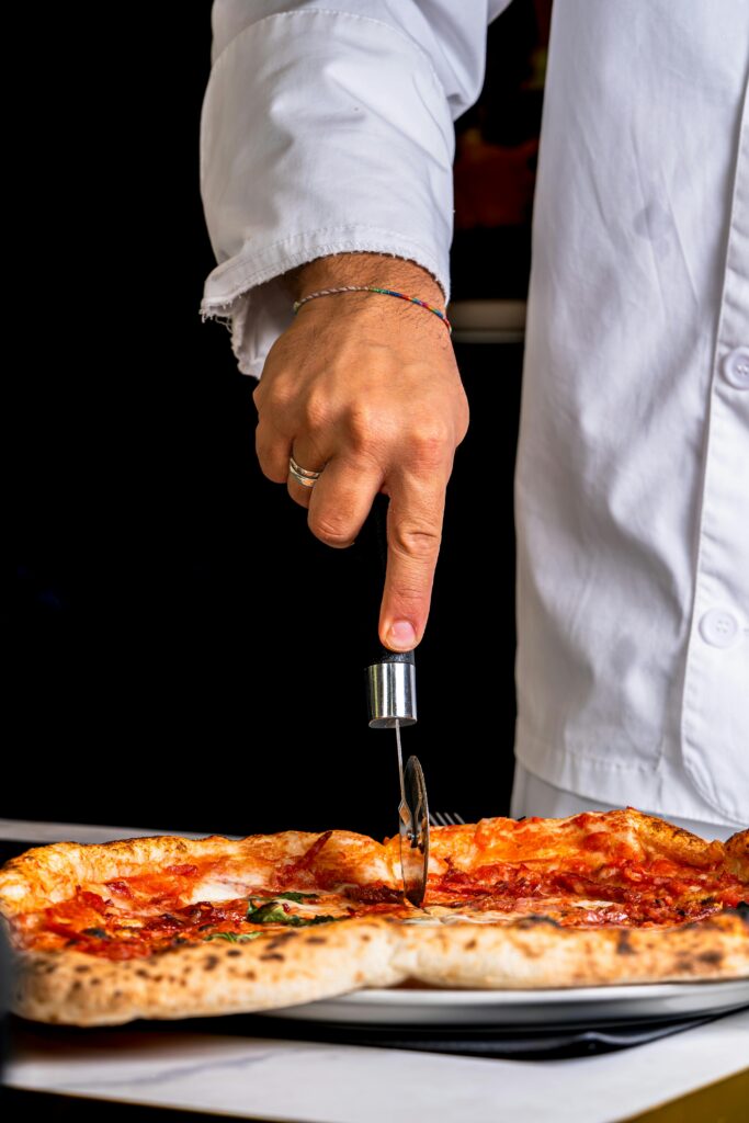 Chef slicing a freshly baked pizza with a cutter in a kitchen setting.