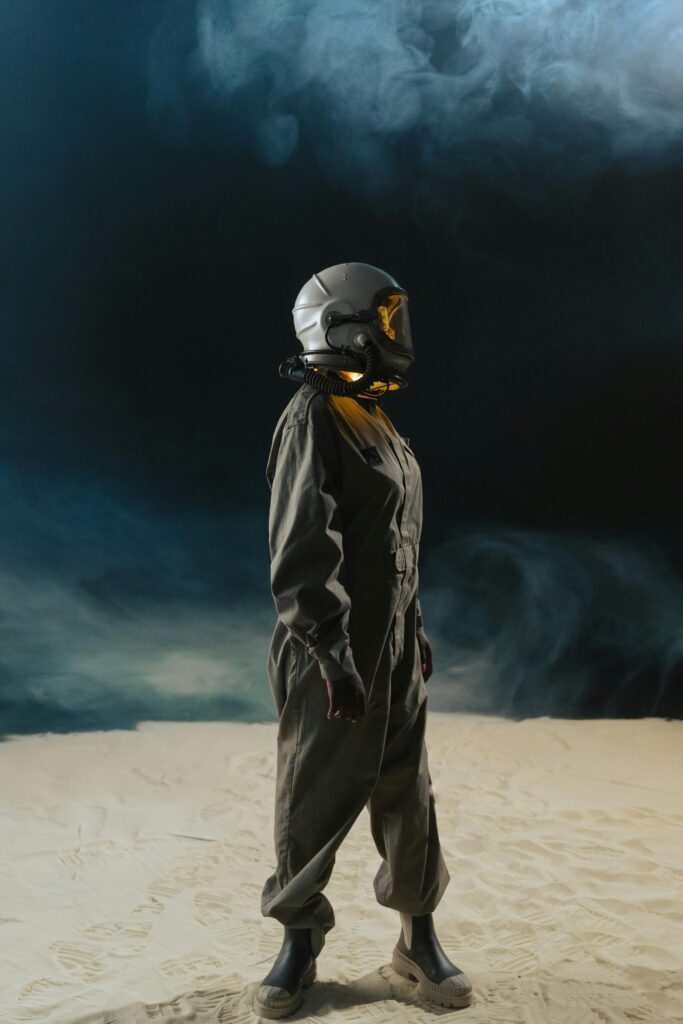 Astronaut in space suit with helmet stands in foggy desert, side view against dark backdrop.