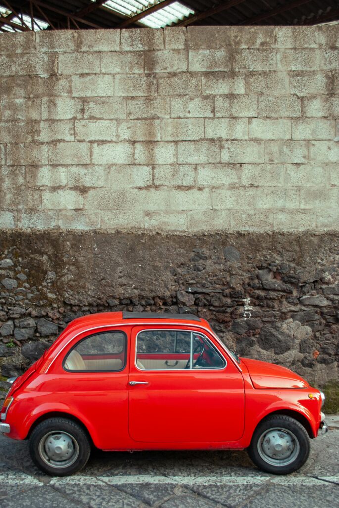 Classic red Fiat 500 parked against a rustic wall in Napoli, Italy, evokes retro charm.